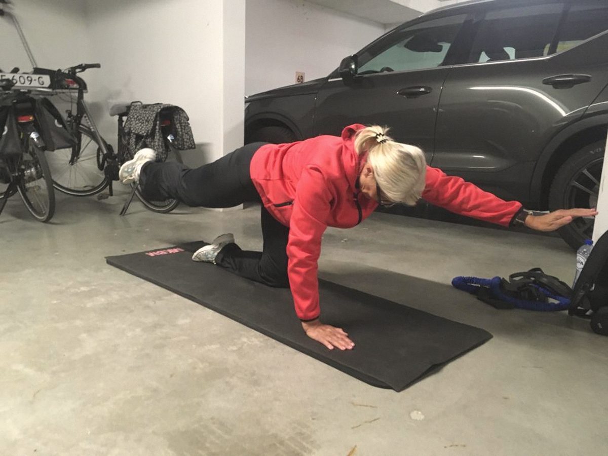 Iemand traint op een mat in een garage naast een geparkeerde auto